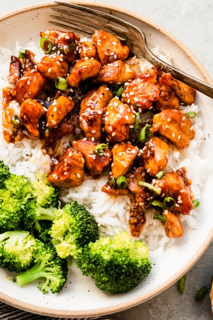 Healthy sesame chicken served with white rice and cooked green beans, topped with sesame seeds.