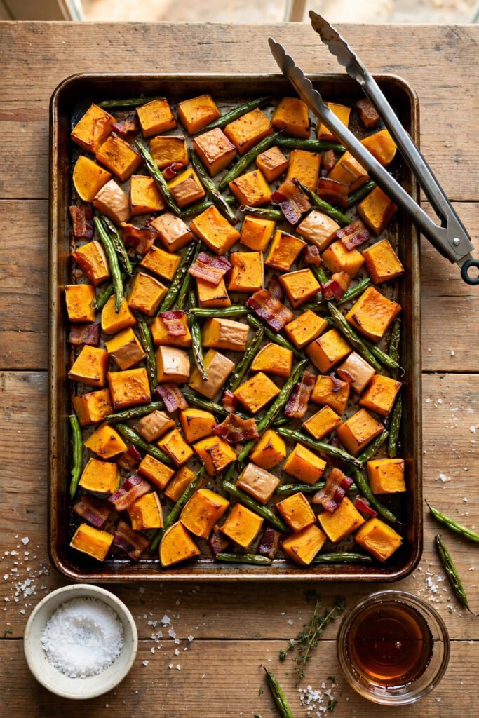 Sheet pan of roasted butternut squash and green beans from above with serving tongs